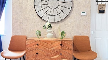 A modern room with a herringbone-patterned wooden dresser, two matching chairs, a large wall-mounted circular artwork, and a door with a welcome sign.