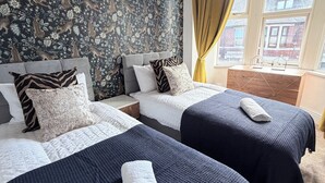 Quarto de hotel com duas camas, papel de parede estampado, janela com cortinas e vista para edifícios.