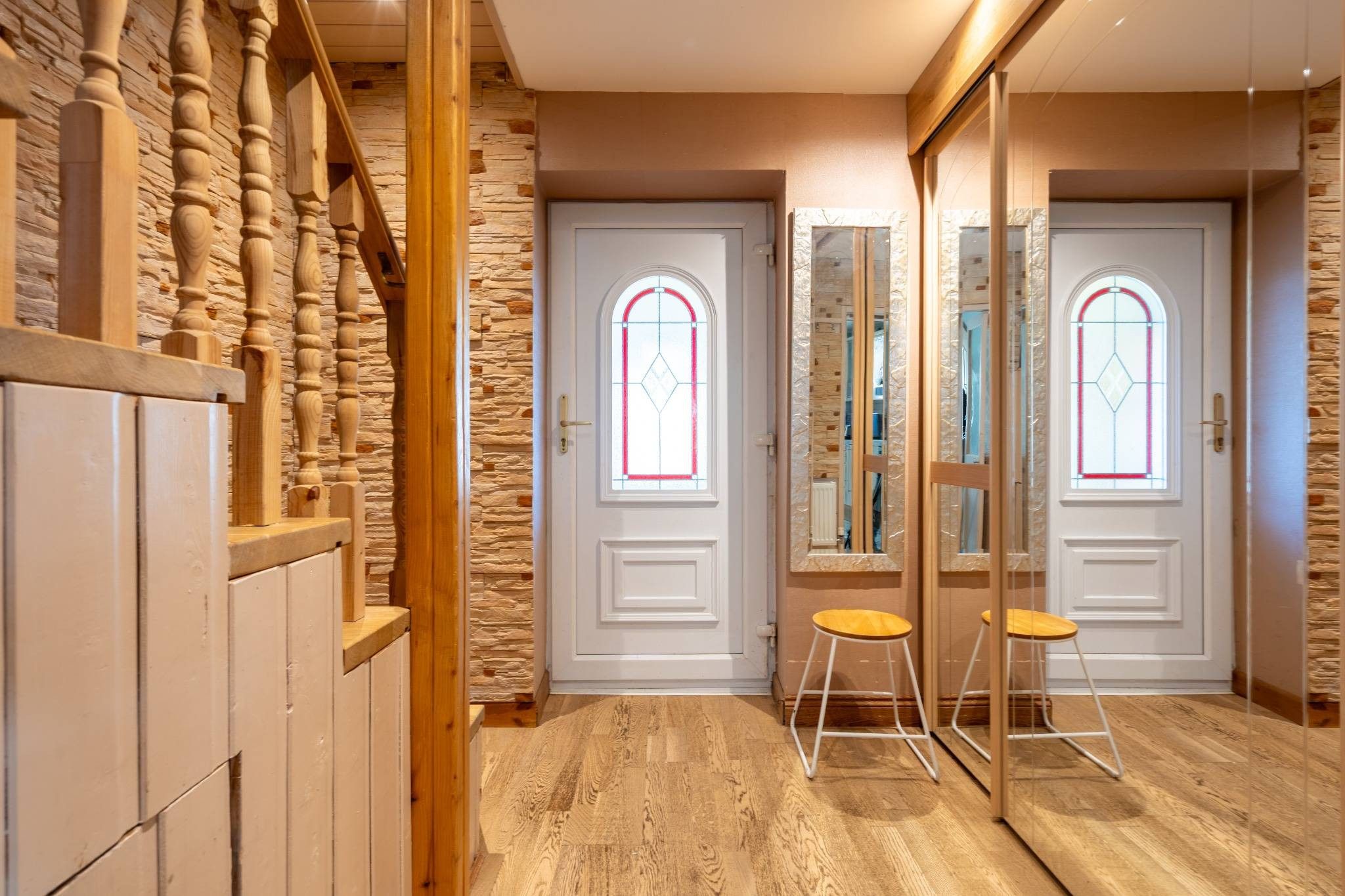 Un couloir doté d’un plancher en bois, d’un mur en pierre et de deux portes blanches ornées de vitraux.