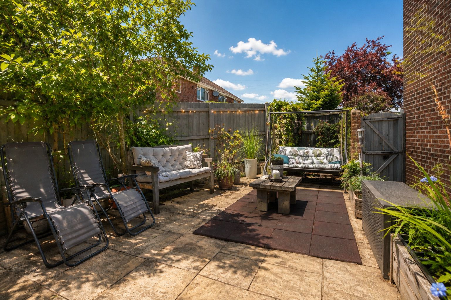 Un espace patio aménagé avec un canapé, deux fauteuils, une petite table et une plante en pot.
