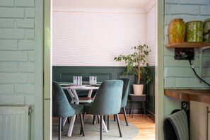 A dining area with a table set for four, two chairs on each side, a potted plant, and a shelf with jars. - K Suites - Liverpool Road (Worcester)