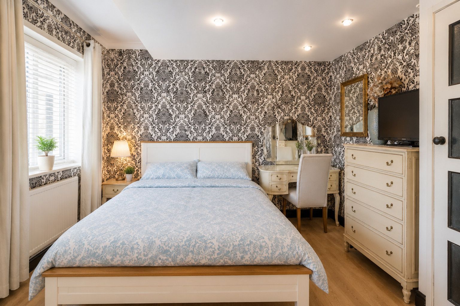 A bedroom with a bed, dresser, desk, and a television.