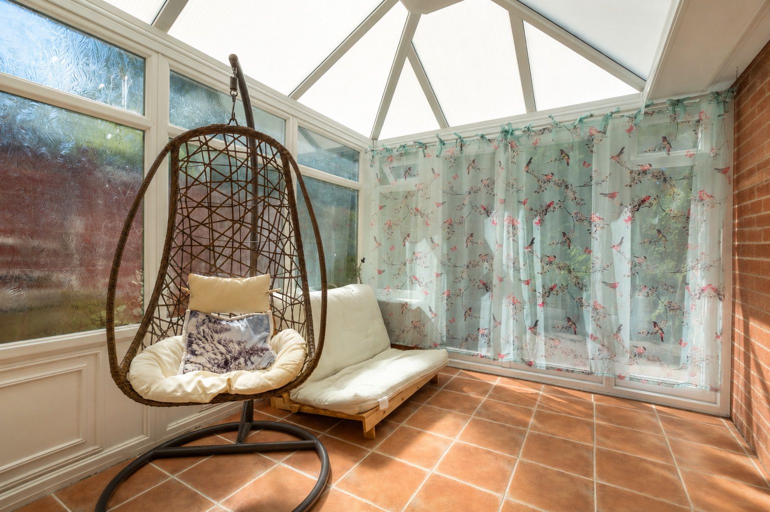 Una habitación con una silla colgante, un sofá y un ventanal con cortinas.