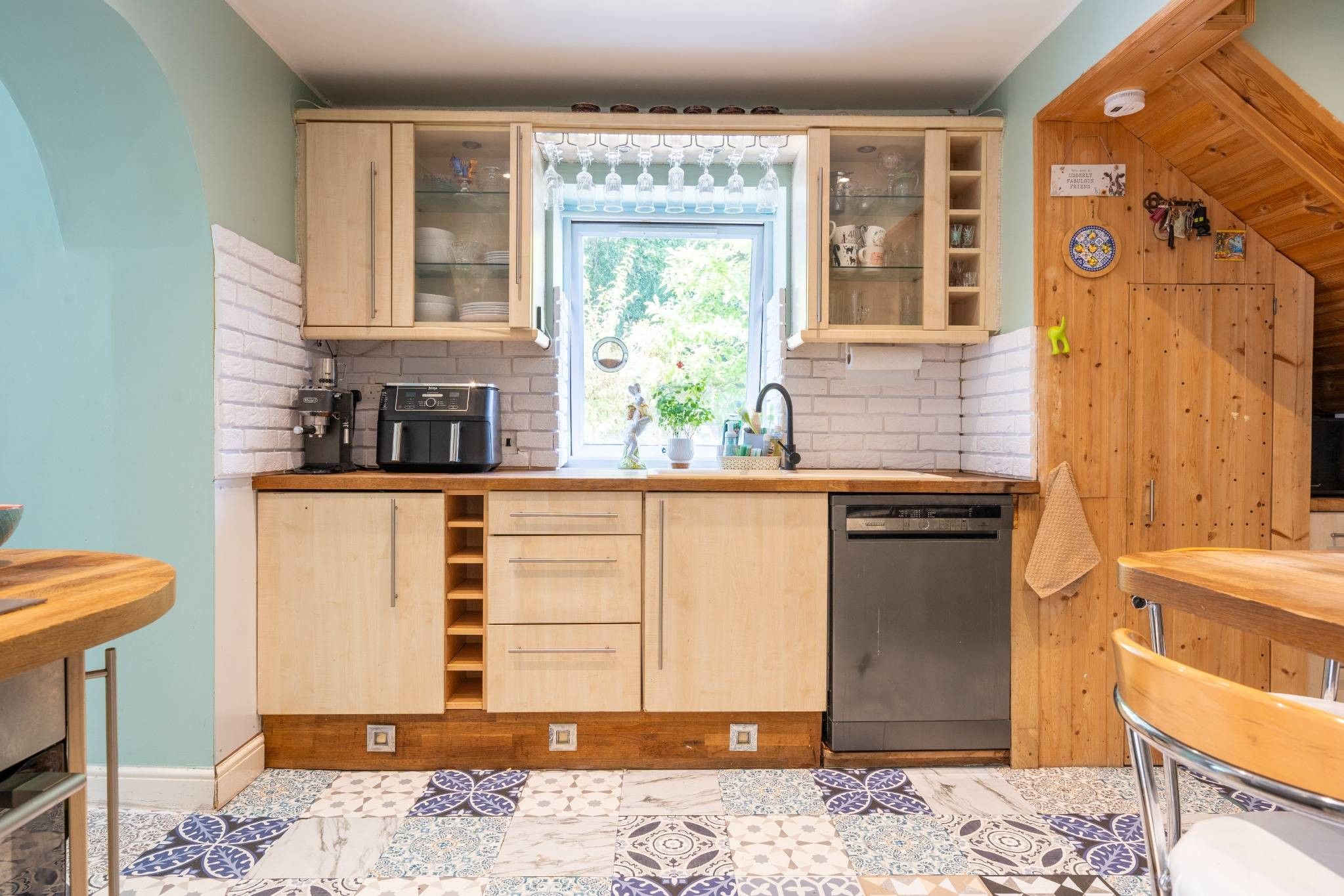 Una cocina compacta con muebles de madera, lavavajillas integrado y ventana con vistas al verdor.