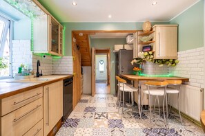 A kitchen with a white brick backsplash, wooden cabinets, a tiled floor, and a dining area with bar stools.