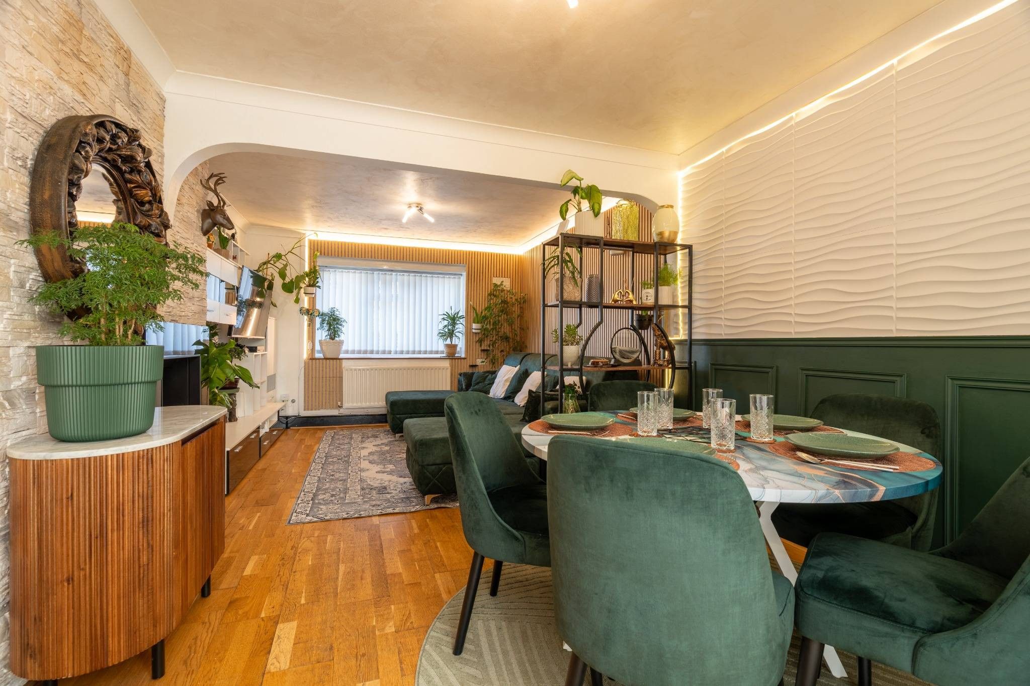 Un espace repas moderne avec une table ronde, des chaises recouvertes d’un tissu vert et une variété de plantes.