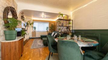 Un espace repas moderne avec une table ronde, des chaises recouvertes d’un tissu vert et une variété de plantes.