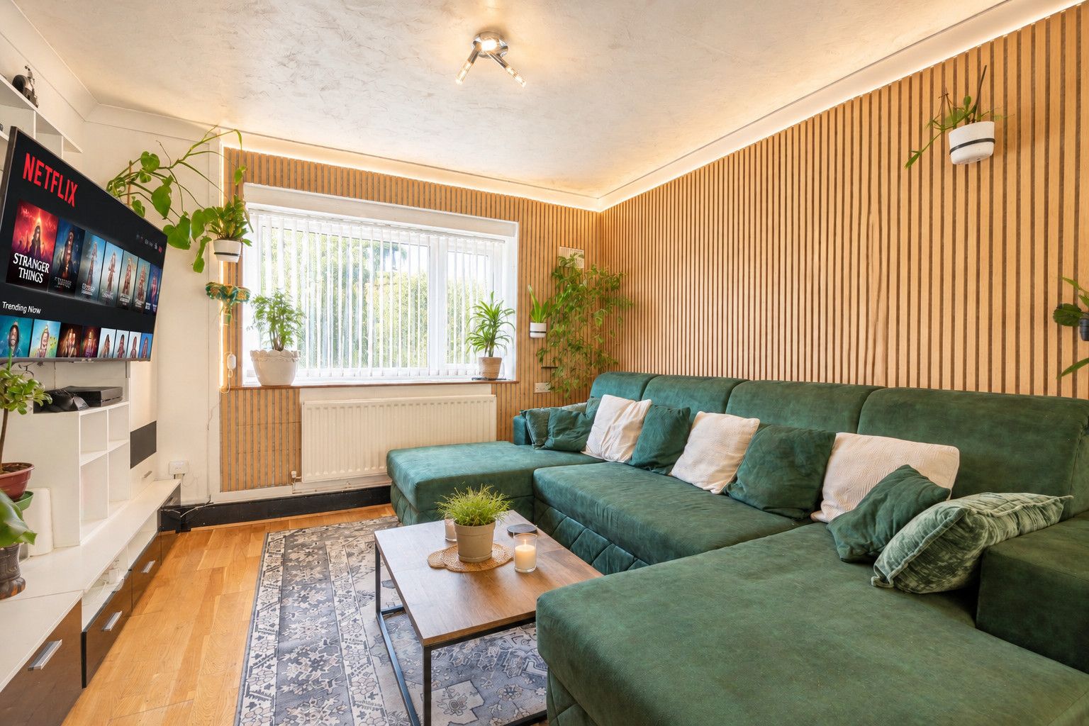 A living room with a green sofa, a coffee table with a candle, and a TV displaying 'Stranger Things'.