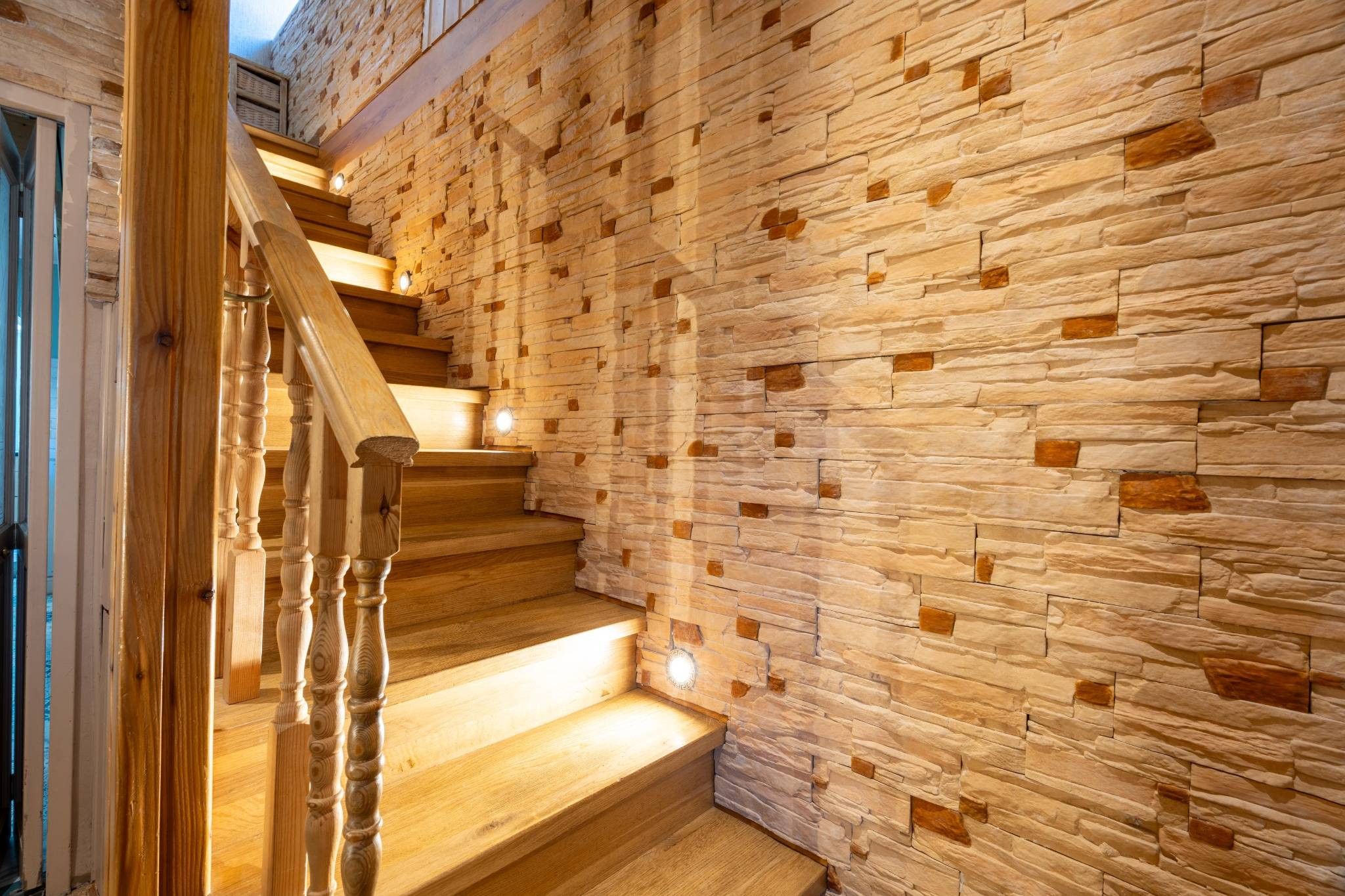 Un escalier en bois, avec un mur de pierre d’un côté.