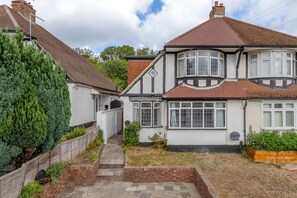 A two-story house with a tiled roof, a bay window, and a front garden with a wooden fence and a large coniferous tree. - Addington Road Croydon (Croydon)