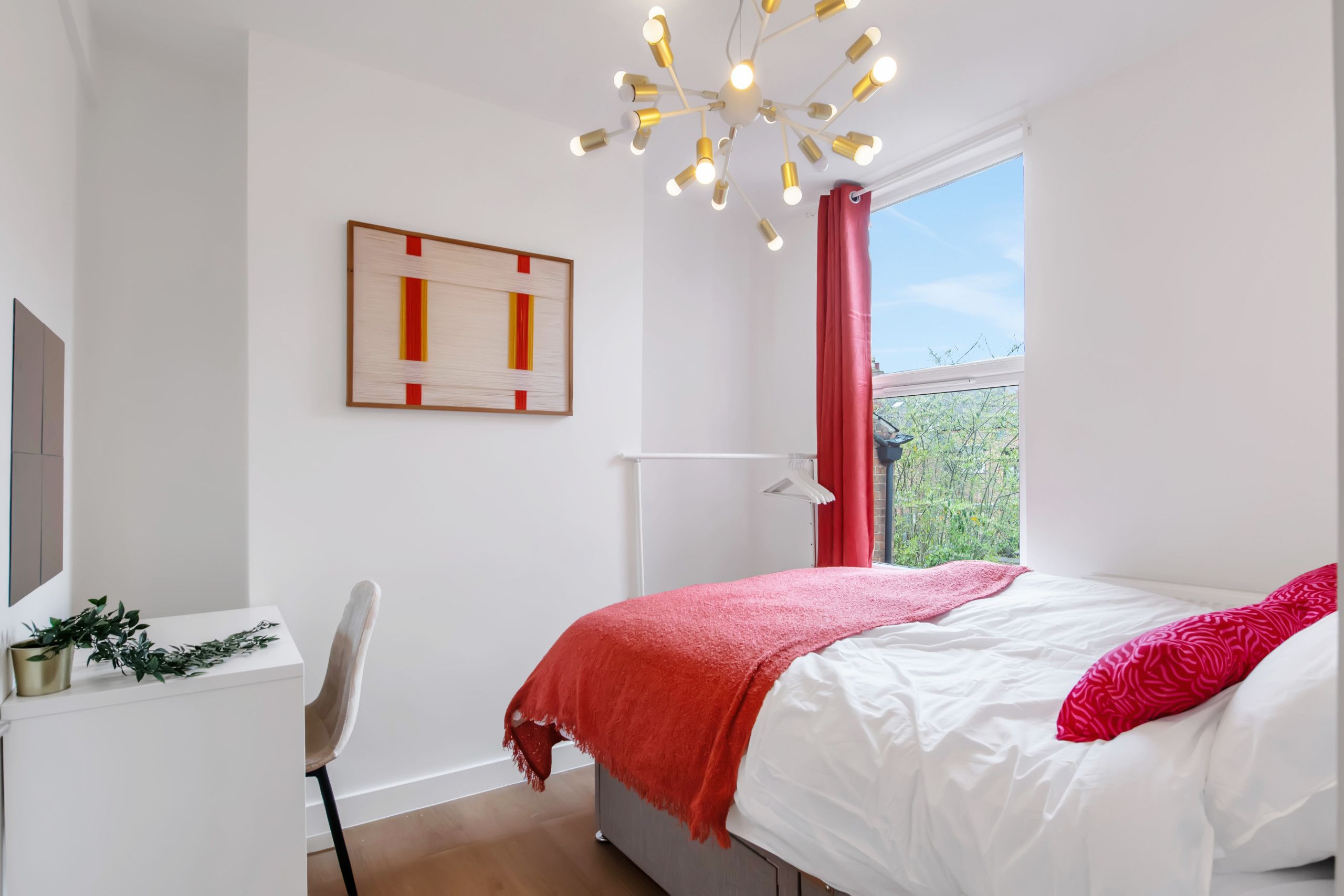 Ein Schlafzimmer mit einem Bett, einem Schreibtisch, einem Stuhl, einem Fenster mit Vorhängen und einer Deckenleuchte.