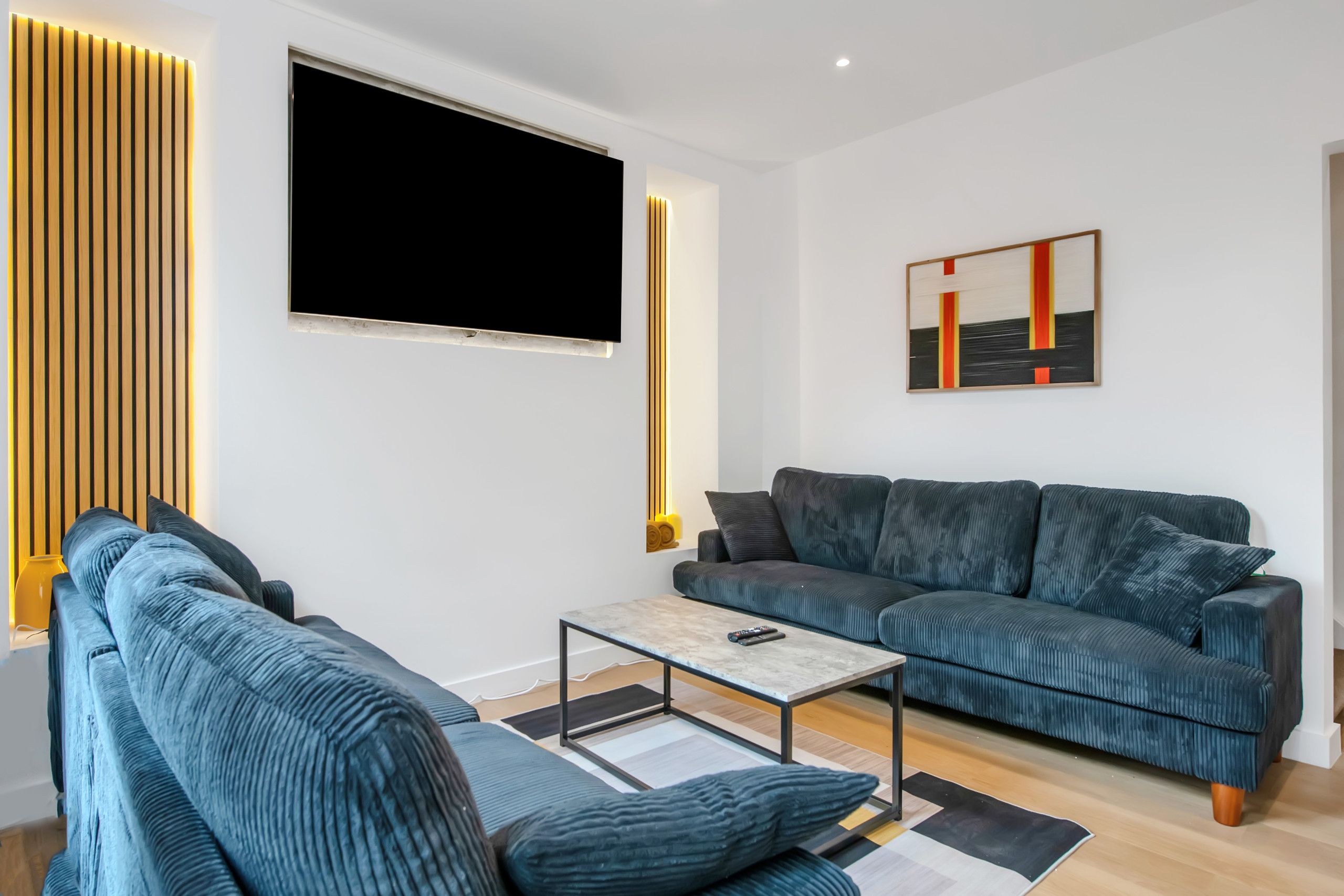Een moderne woonkamer met een bank, een salontafel en een flatscreen televisie aan de wand.