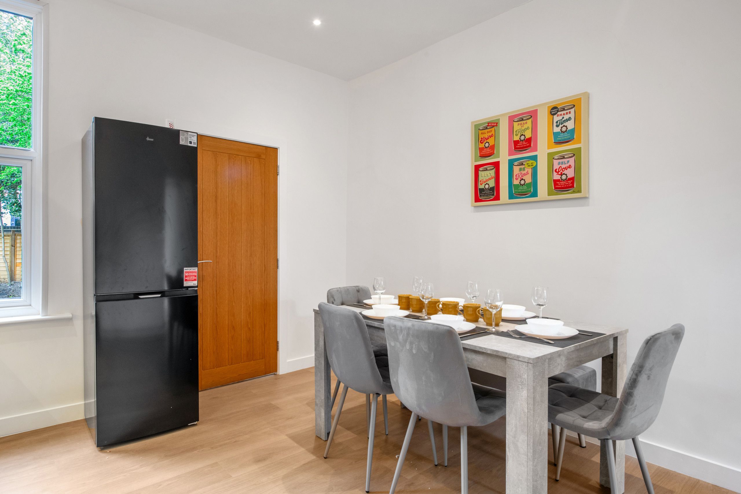 Ein Essbereich mit einem Tisch für vier Personen, grauen Stühlen und einem schwarzen Kühlschrank.