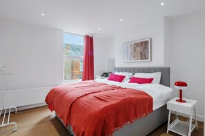 A modern bedroom with a large bed, a bedside table, a radiator, and a window with a view of a brick building. - K Suites - Modern Urban 3 bed House w/ Garden views (Nottingham)