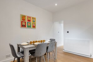 A dining area with a table set for four, four chairs, and a wall-mounted artwork above the table. - K Suites - Modern Urban 3 bed House w/ Garden views (Nottingham)