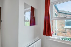 Une pièce avec une fenêtre, un radiateur et une vue sur un immeuble en briques à l’extérieur.