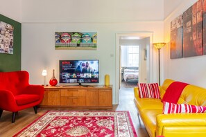 Ein Wohnzimmer mit Fernseher, roten und gelben Sofas, einem Holzkabinett und einem gemusterten Teppich.
