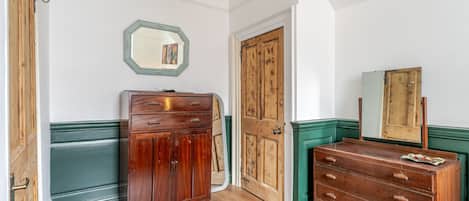 A room with a wooden wardrobe, a green dresser, and a mirror on the wall.