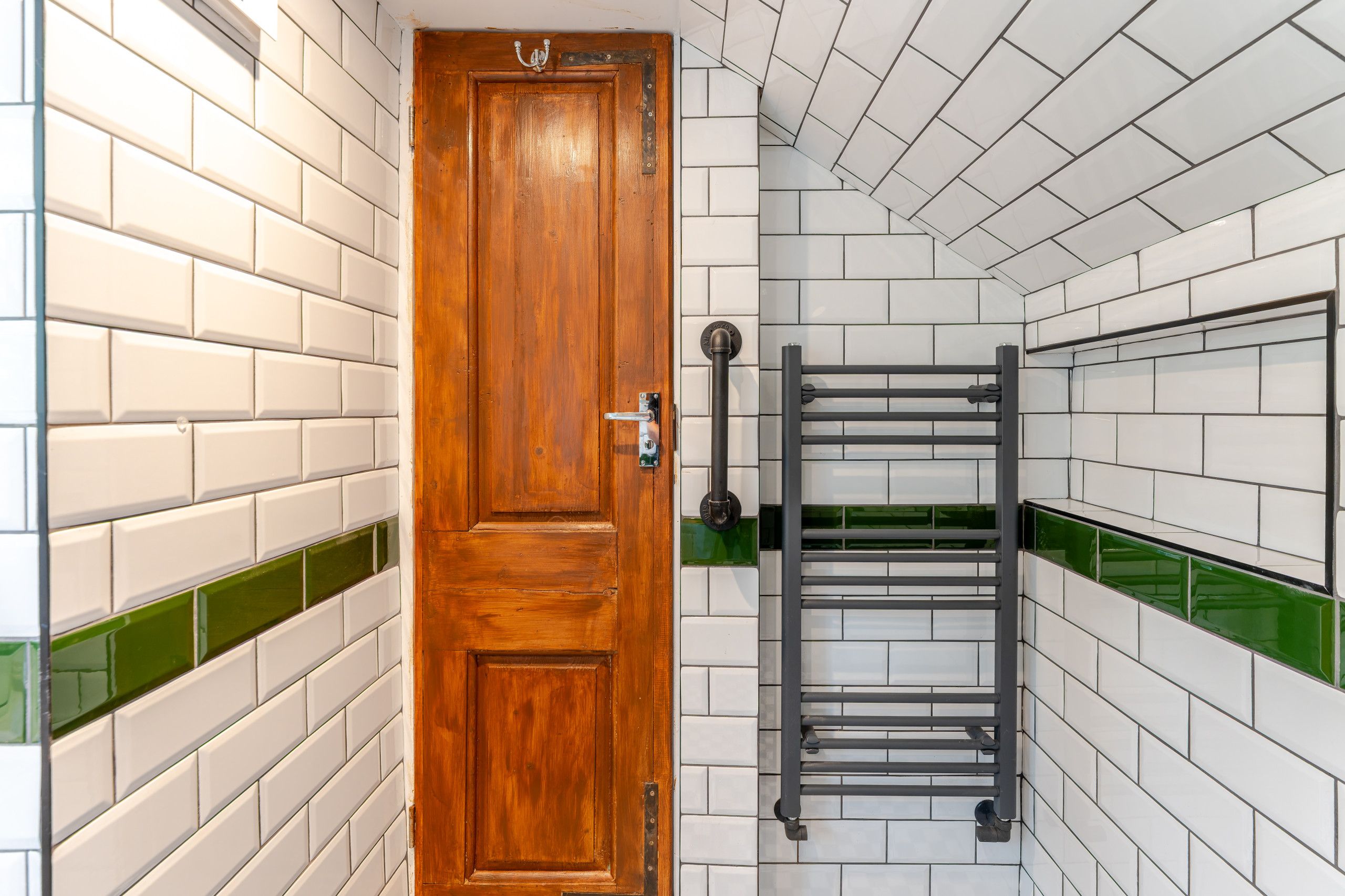 A wooden door with a metal handle, a towel rack, and white tiled walls with green accents.