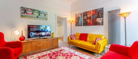 A living room with a television, a sofa, a red rug, and artwork on the walls.