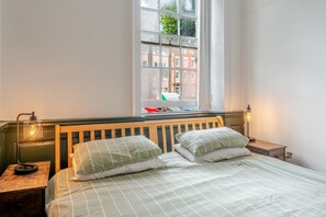 Ein Schlafzimmer mit Bett, Nachttischen, einem Fenster mit Blick auf Gebäude und einer Lampe.