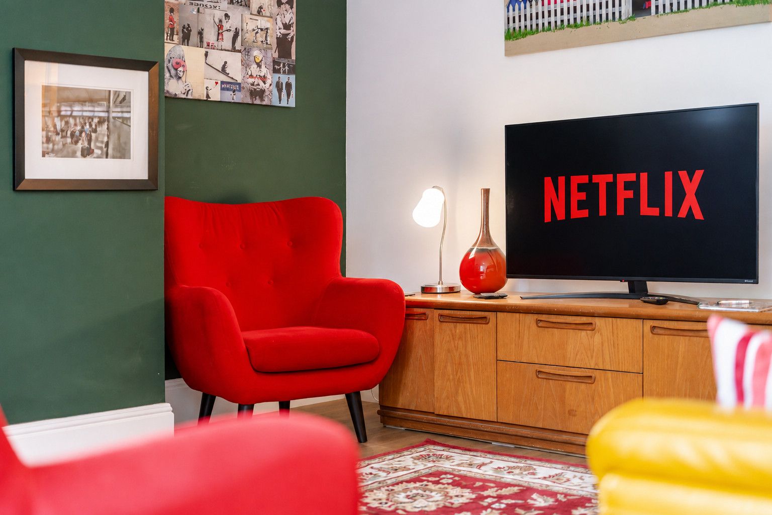 A room with a red armchair, a wooden cabinet, a television displaying 'NETFLIX', and a framed picture on the wall.