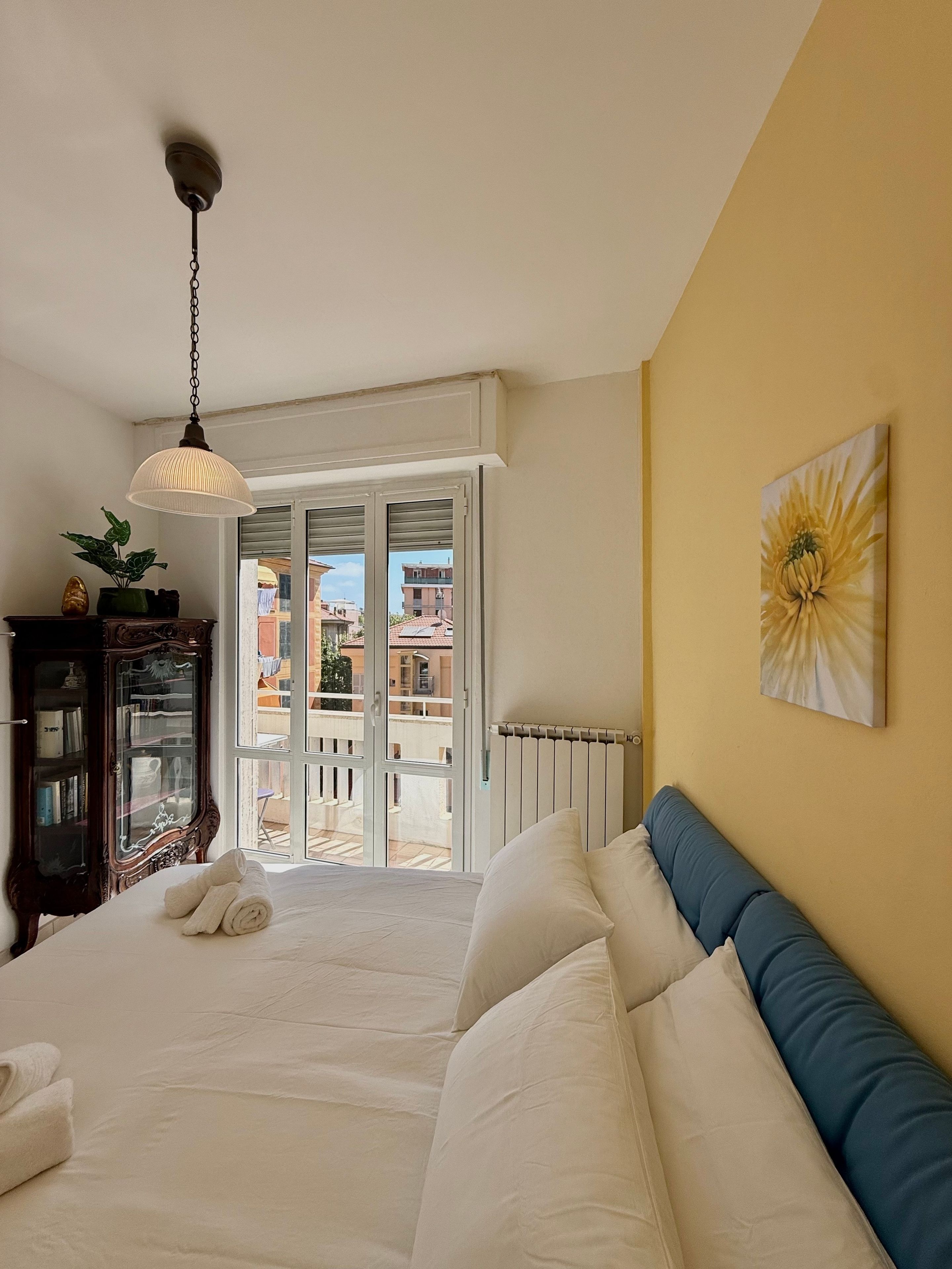 Un dormitorio con cama, un radiador, una ventana y vistas a edificios.