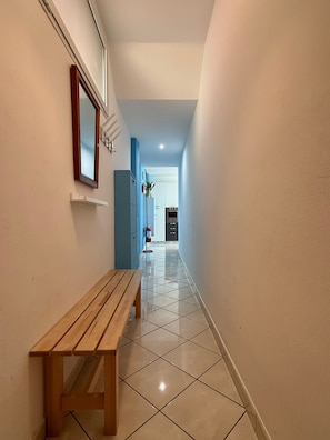 Un pasillo con un banco de madera, un extintor y vistas a una habitación con zona de cocina.