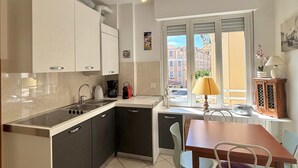 A modern kitchen with a central island, a dining area with a table and chairs, and a view of buildings through a window. - Apartment 'Casa Di Fiorentino' with Balcony, Wi-Fi and Air Conditioning (Sanremo)