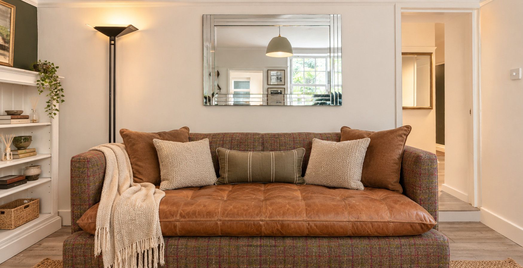 A brown leather sofa with multiple cushions, a floor lamp, and a mirror on the wall.