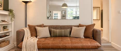 A brown leather sofa with multiple cushions, a floor lamp, and a mirror on the wall.