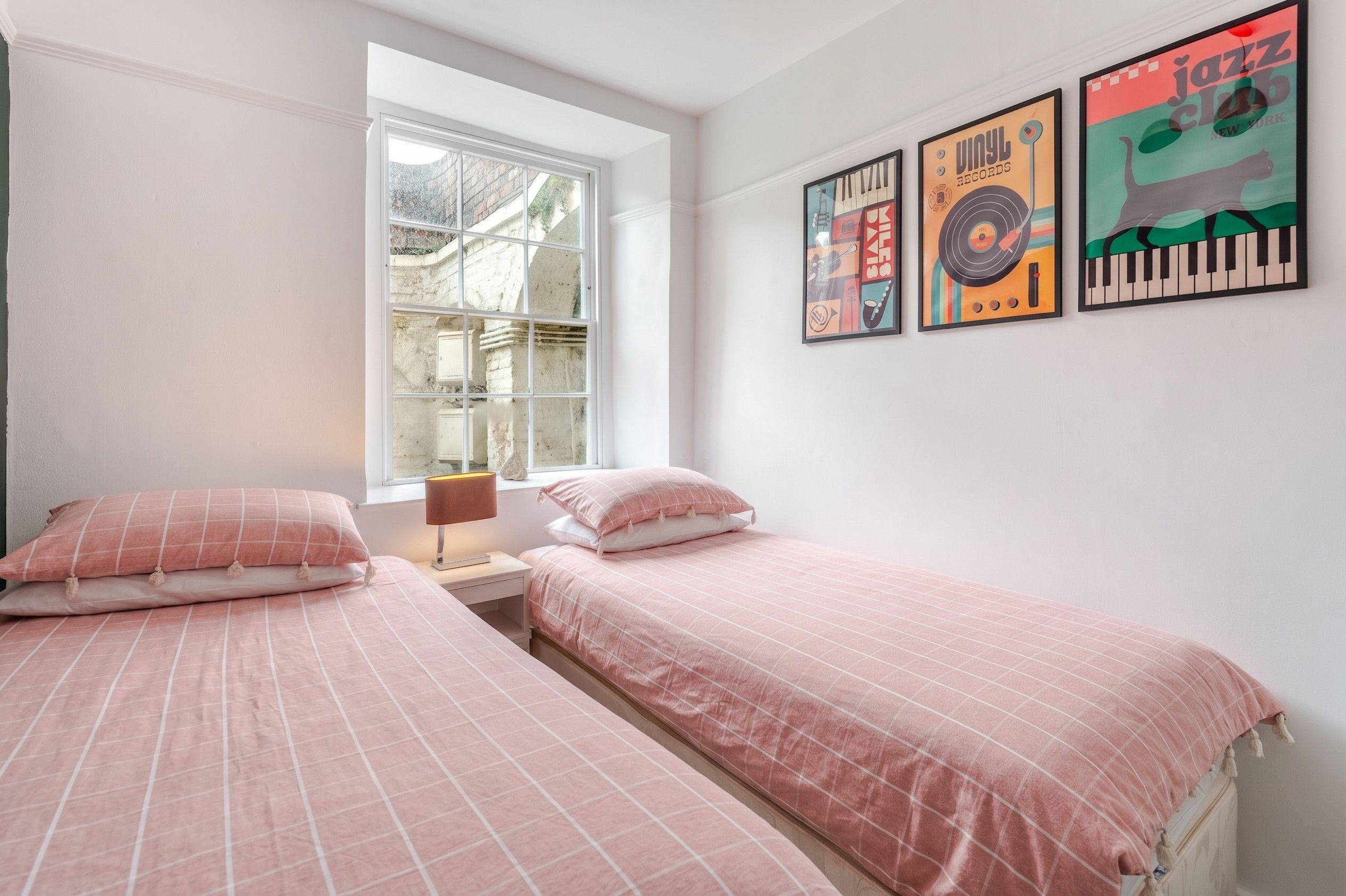 A bedroom with two beds, a window, and three wall posters.