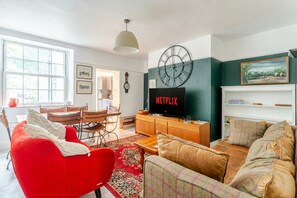 Ein Wohnzimmer mit einem roten Sessel, einem braunen Sofa, einem Holz-TV-Schrank und einer Wanduhr.