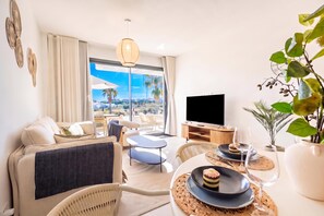 A modern living room with a large TV, comfortable seating, a dining area with a dessert, and a view of the outdoors. - Bahia La Cala Paradise And Sunshine (Mijas)