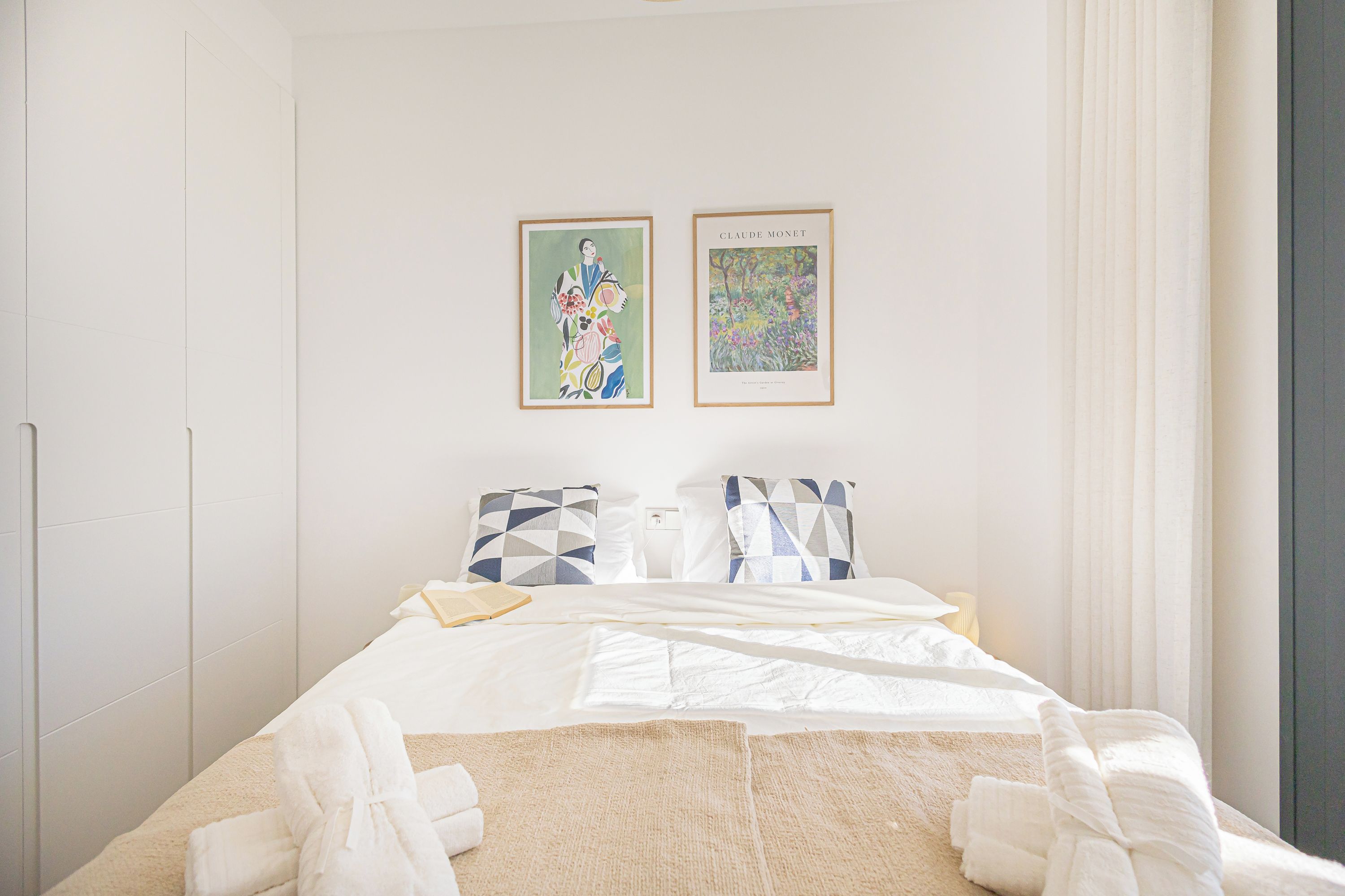 A hotel room with a bed, two pillows, a blanket, a robe, and two framed artworks on the wall.