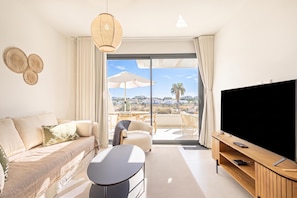 Ein modernes Wohnzimmer mit einer Couch, einem Couchtisch, einem Fernseher und einem Balkon mit Aussicht.