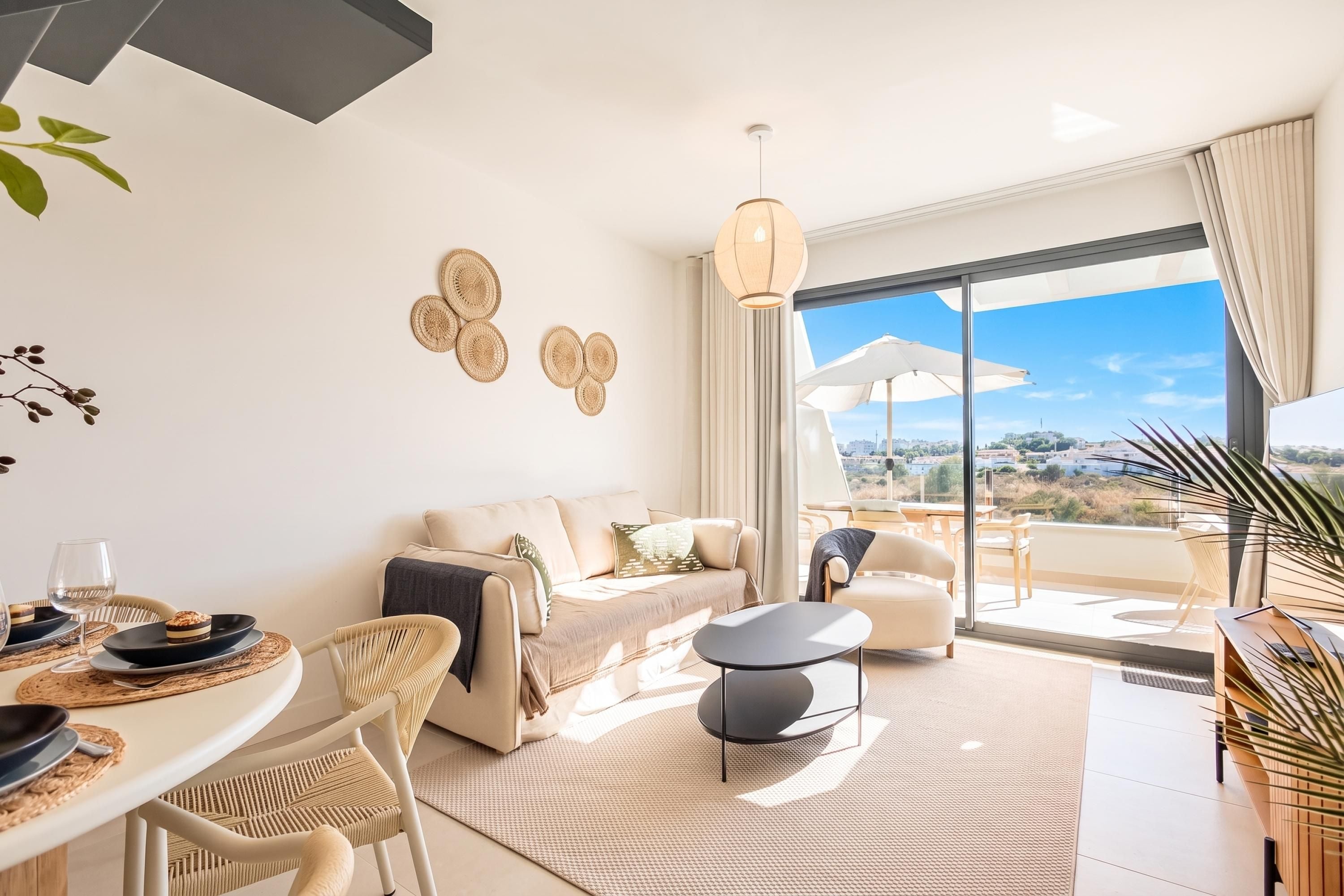 Una sala moderna con sofá, mesa de comedor y sillas, un balcón con vistas, y decoración en la pared.