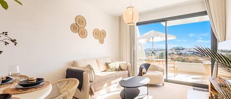 Una sala moderna con sofá, mesa de comedor y sillas, un balcón con vistas, y decoración en la pared.