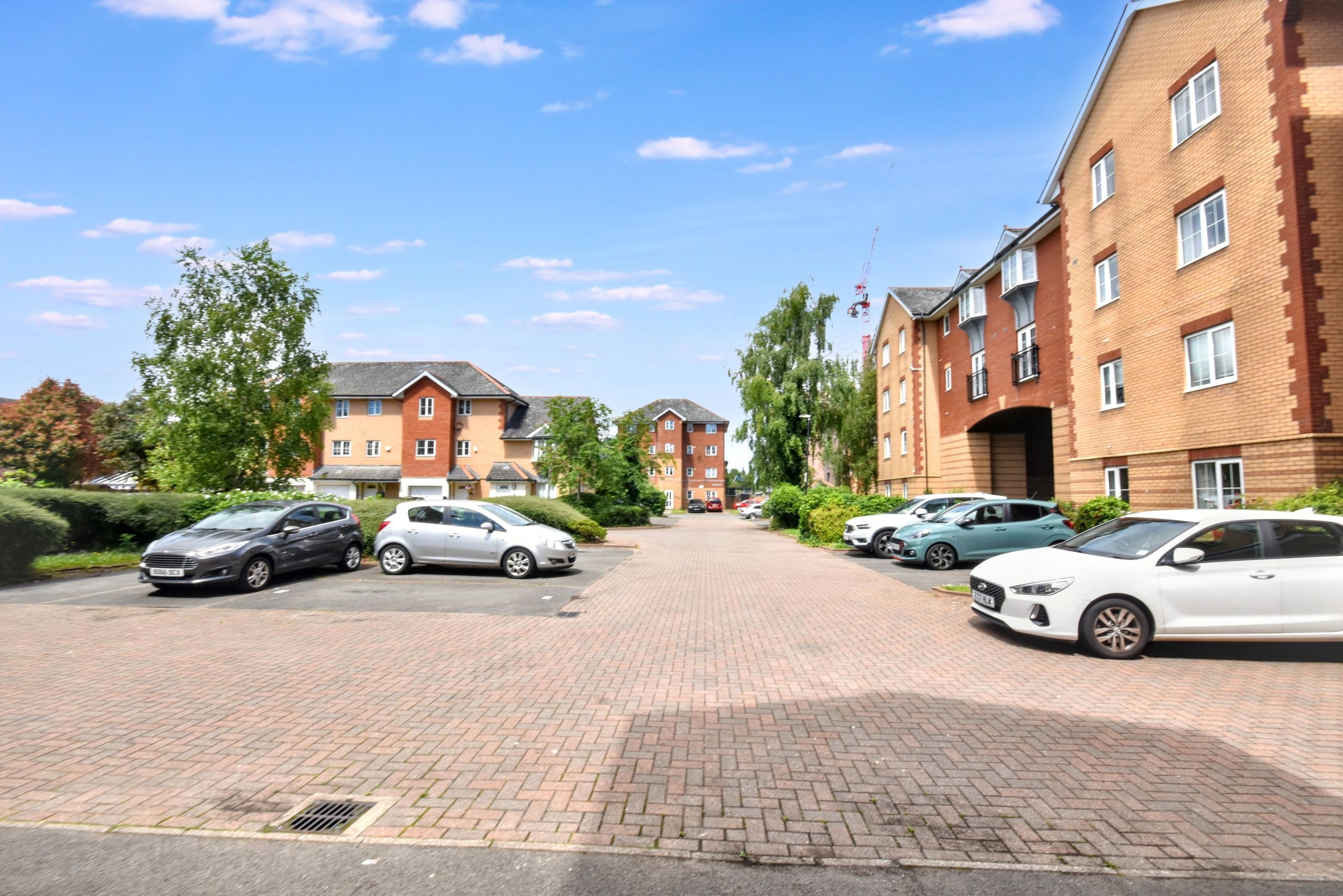 A residential area with brick buildings, a paved driveway, and parked cars.