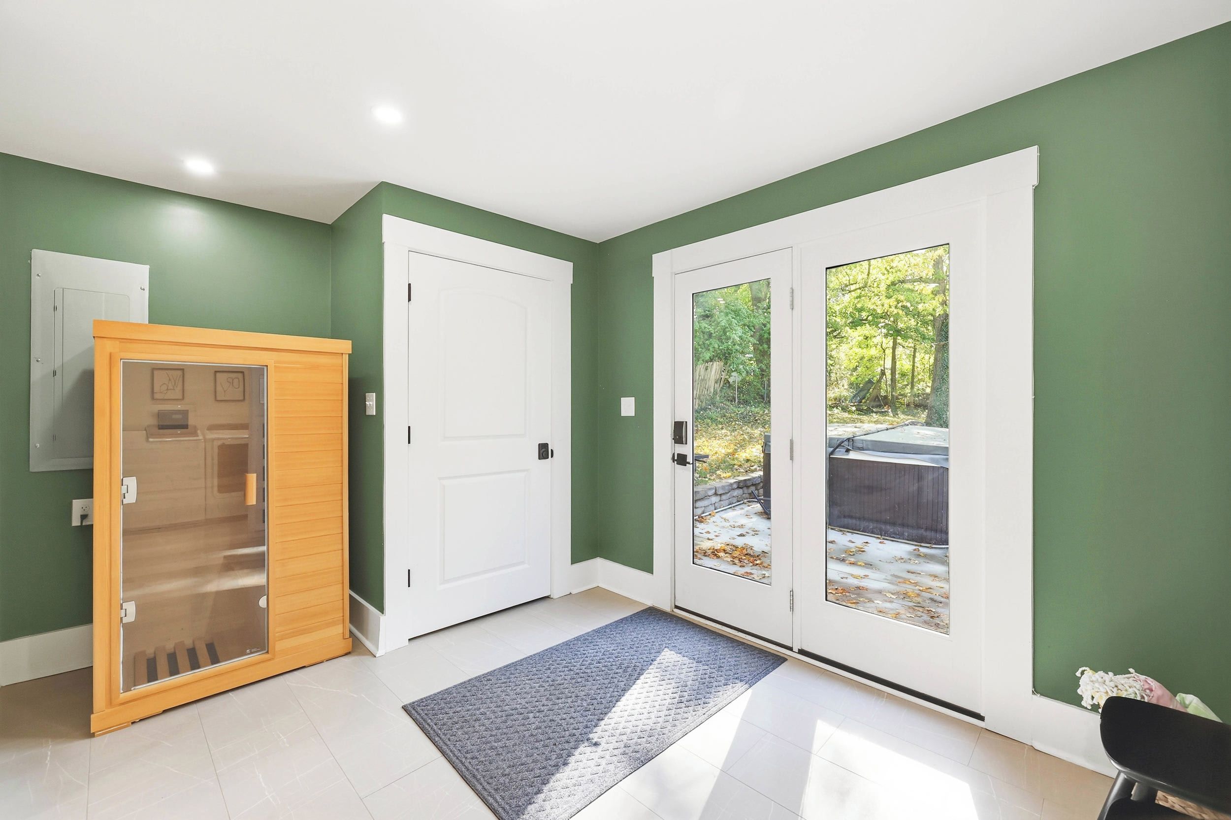 Un pasillo con una puerta de madera, una puerta blanca y una puerta de vidrio que da a un área exterior con vistas a árboles y un patio.