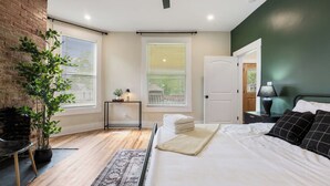 Een slaapkamer met een bed, nachtkastje, lamp, potplant en een raam met jaloezieën.