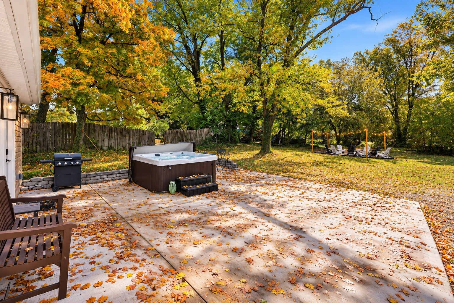 An outdoor patio with a hot tub, a grill, and a seating area with chairs.