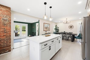 Una cocina moderna con una isla grande, un comedor con candelabro y una pared de ladrillo.