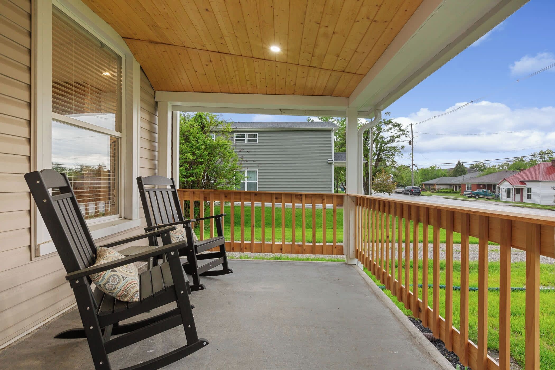 A covered porch with two rocking chairs, a wooden railing, and a view of a residential street.