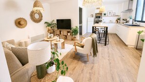 Una sala de estar moderna con sofá, mesa de centro y televisor, comunicada con una cocina y zona de comedor.