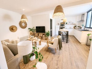 Ein modernes Wohnzimmer mit Sofa, Couchtisch und Fernseher, verbunden mit einer Küche mit Essbereich.