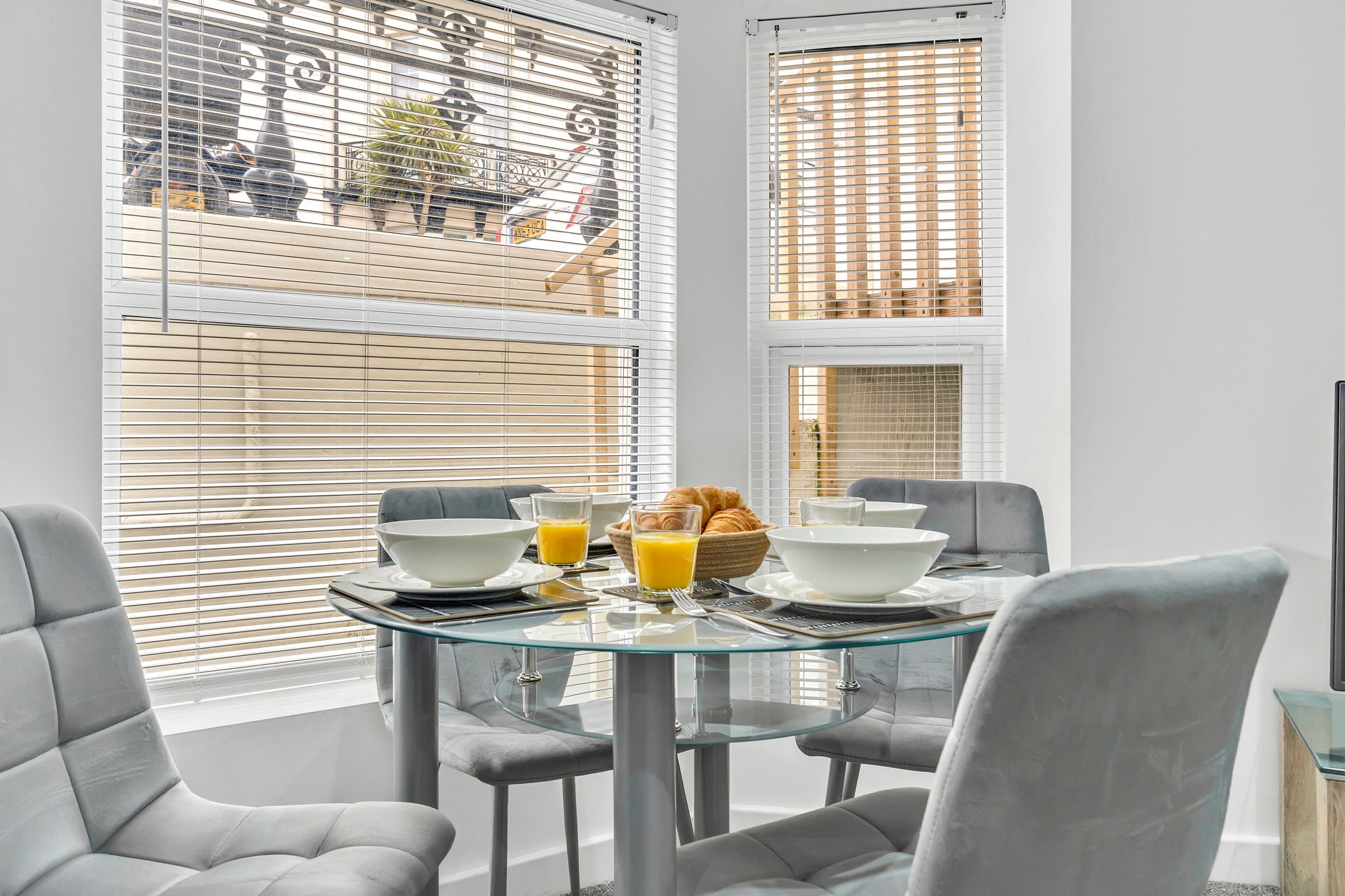 A dining area with a glass table, grey chairs, and breakfast items.