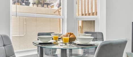 A dining area with a glass table, grey chairs, and breakfast items.