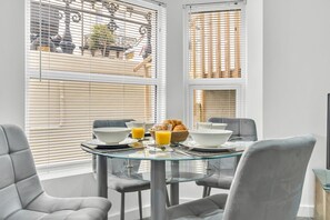 Un comedor con mesa de vidrio, sillas grises y productos para el desayuno.