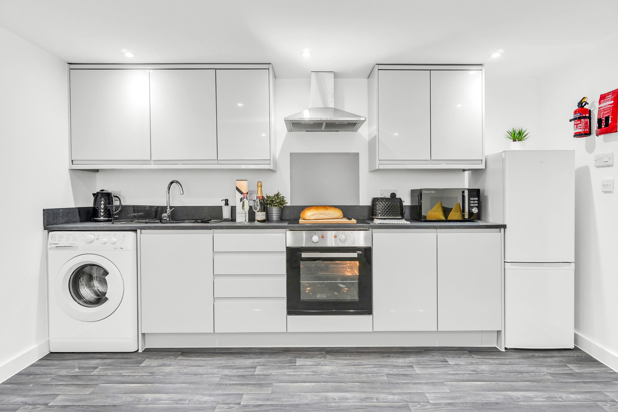A modern kitchen with white cabinets, a washing machine, an oven, and a microwave.